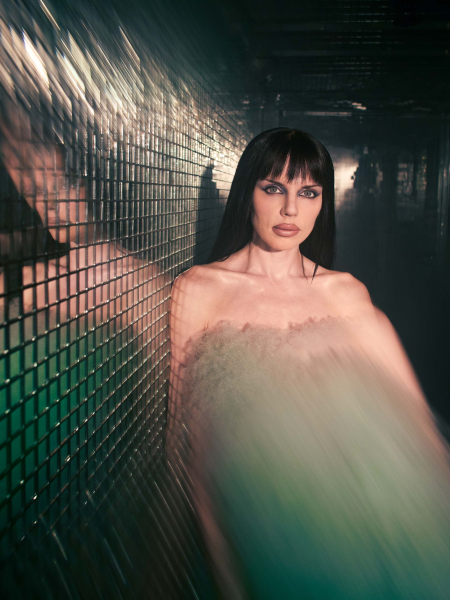 Julia fox in green dress standing in mirrored hallway.